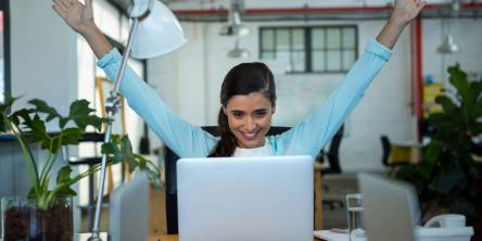 Female business executive celebrating success while looking at laptop in modern office